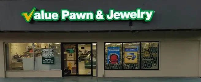 Value Pawn & Jewelry store exterior at night, with illuminated green and yellow signage and window displays advertising cash loans and layaway.