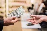 Customer receiving cash bills from a store associate across a retail counter.