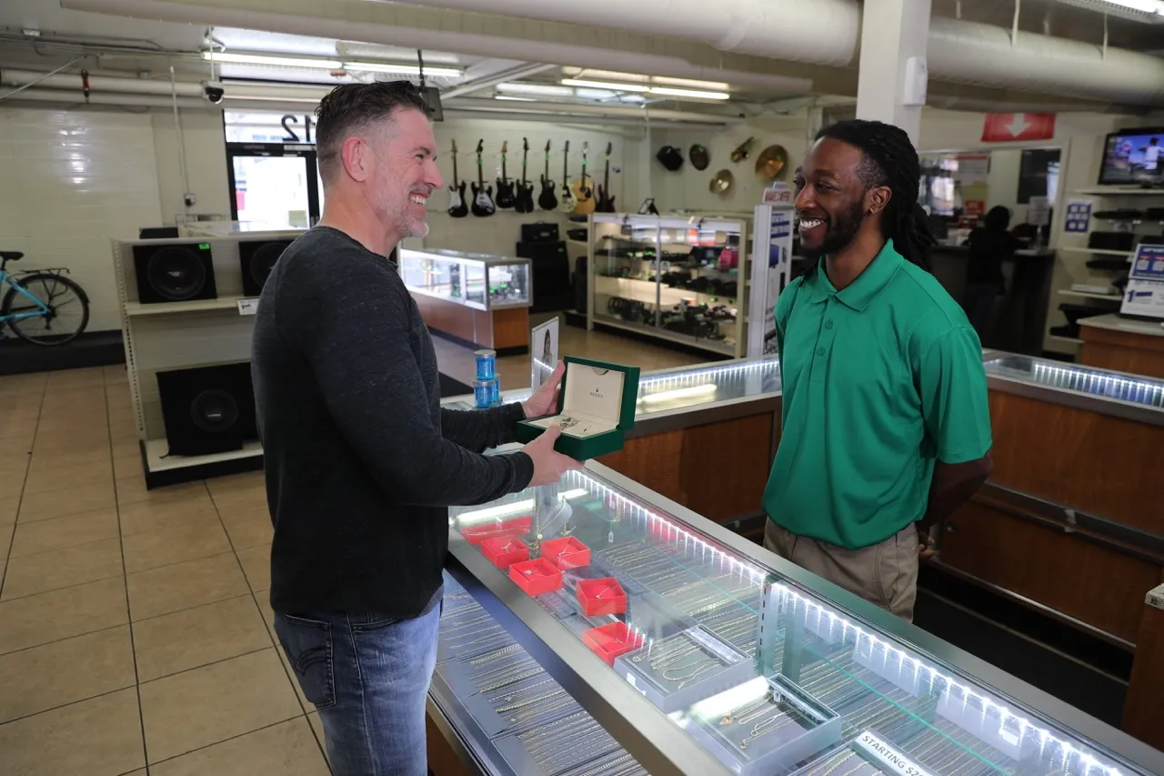 A customer holding a watch in Value Pawn & Jewelry pawn shop, likely discussing or finalizing the purchase of the watch with a store Team Member.