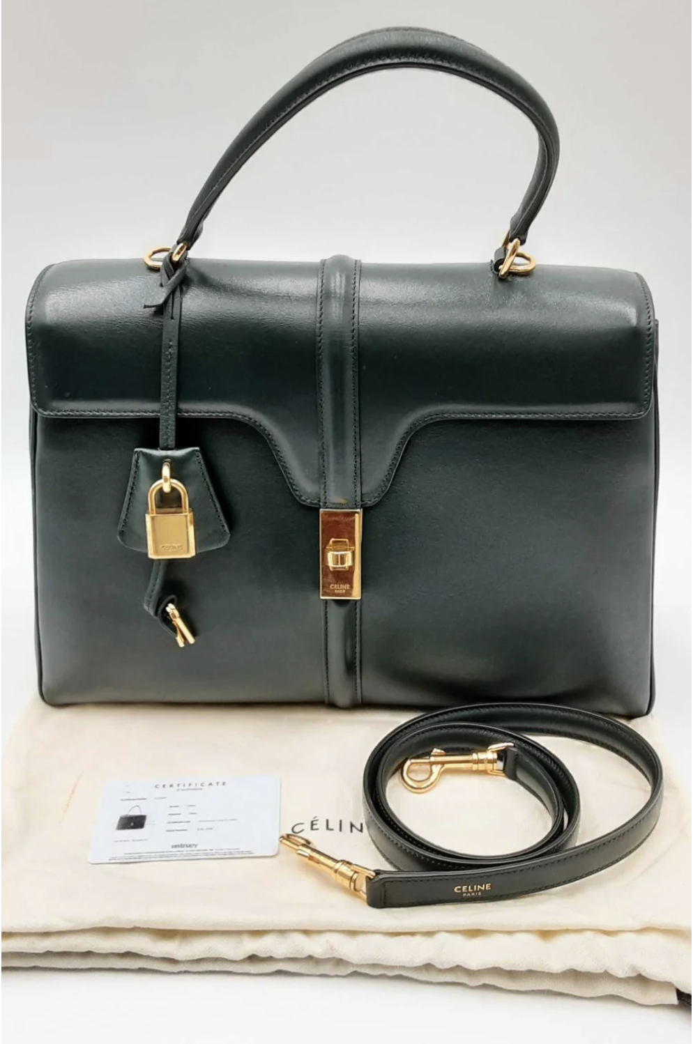 A black Celine designer handbag with gold locks and keys, a detachable strap, and a certification card displayed on a beige cloth, indicating its authenticity.