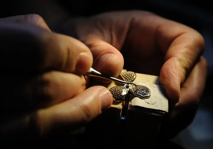 A close-up of a pawn jeweler inspecting and or evaluation a gold piece of jewelry. The jeweler’s hand and a specialized tool are in the frame.