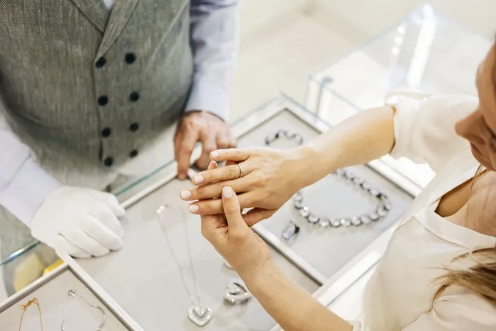 A customer trying on a ring in a jewelry store, with a salesperson assisting.