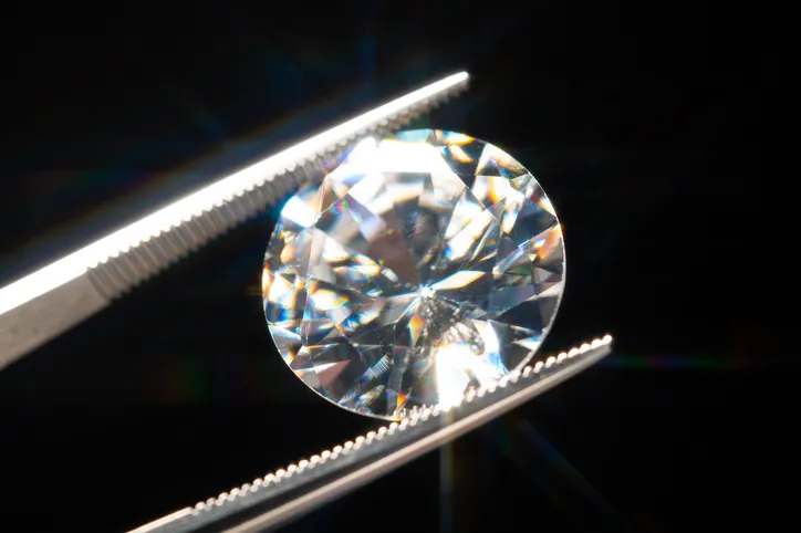 A close-up of a brilliantly sparkling round cut diamond held by tweezers.