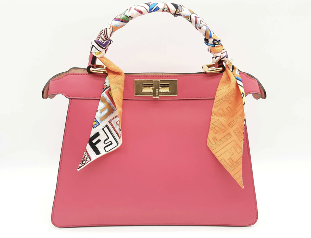 A bright pink Fendi designer handbag with a gold clasp and a colorful scarf tied to one handle.