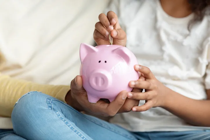 A close-up of a child placing a coin into a pink piggy bank, highlighting the concept of saving money and financial literacy from a young age.