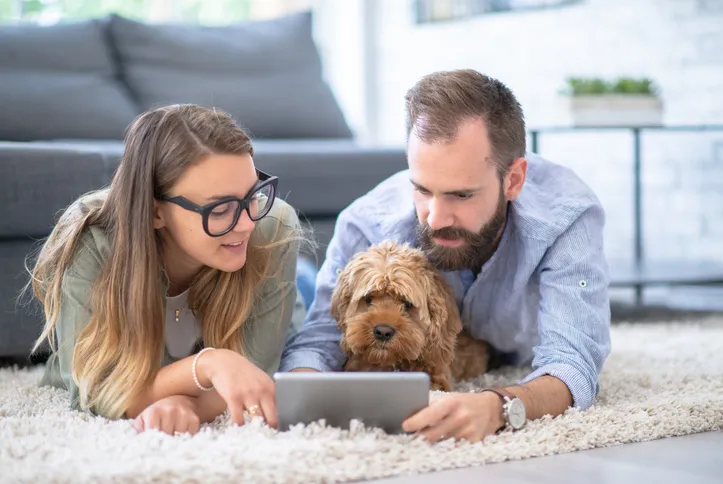 A couple lying on the floor with their dog, looking at a tablet together. This image suggests family bonding, possibly while discussing financial matters or engaging in online activities related to financial planning.