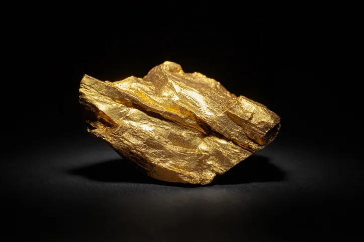 A large gold rock is on display with a black background. It’s spotlighted from the top down showing the contrasting layers of gold.