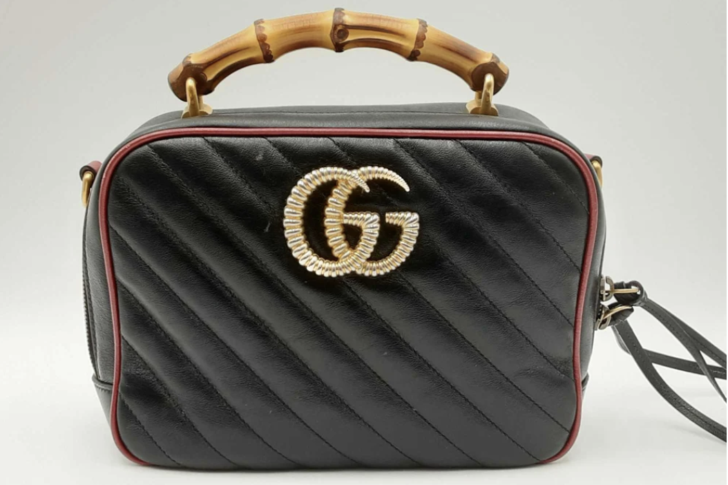 A Gucci black designer handbag with a quilted design and a prominent gold logo, featuring a bamboo handle.