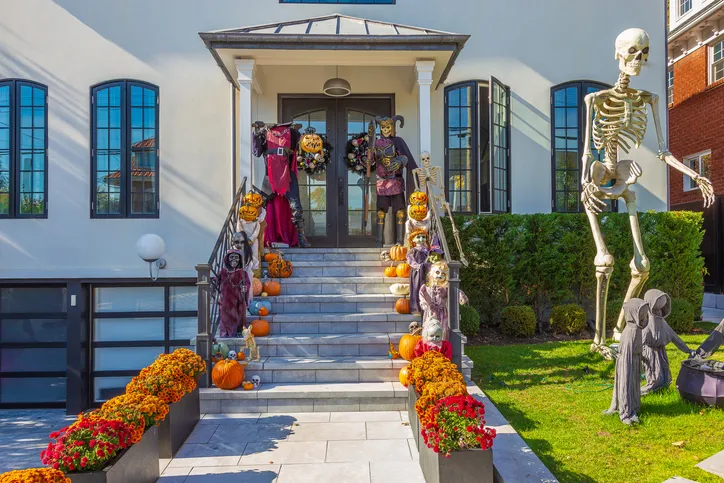 A house decorated for Halloween with various decorations like pumpkins, skeletons, and other spooky elements arranged on the steps and around the entrance.