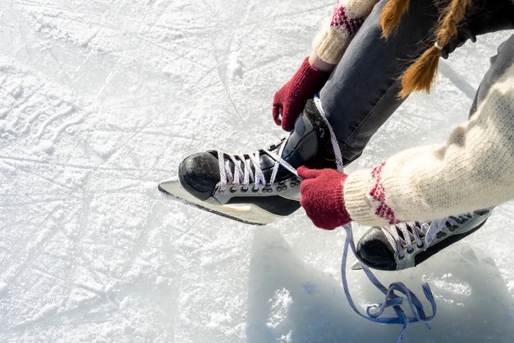 A person tying the laces on a pair of ice skates while sitting on the ice, preparing for skating.