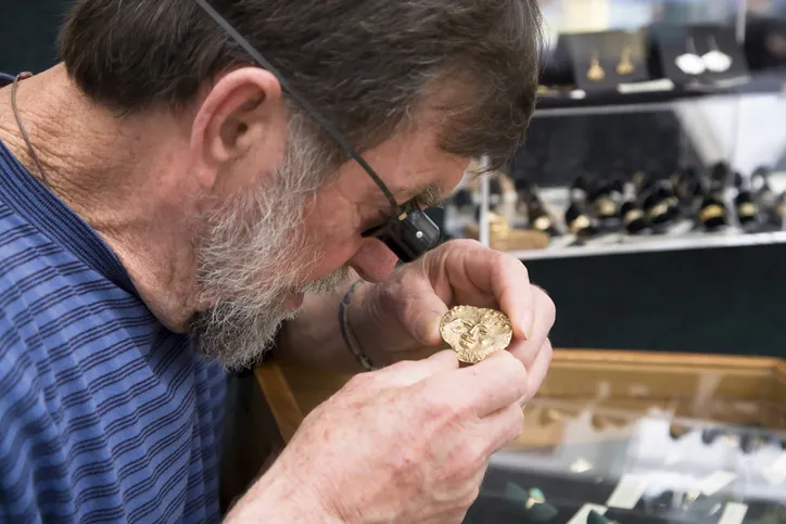 A Value Pawn & Jewelry Team Member inspecting a gold coin using a jeweler's loupe.