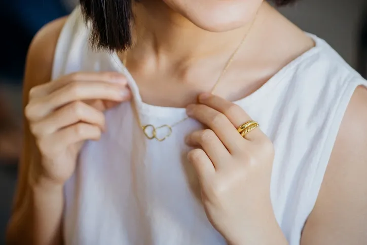 A person wearing a necklace and rings, focusing on how the jewelry is worn and styled.