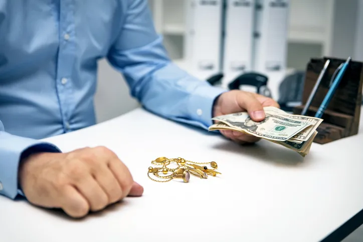 Man in dress shirt holding cash with gold jewelry on the counter.