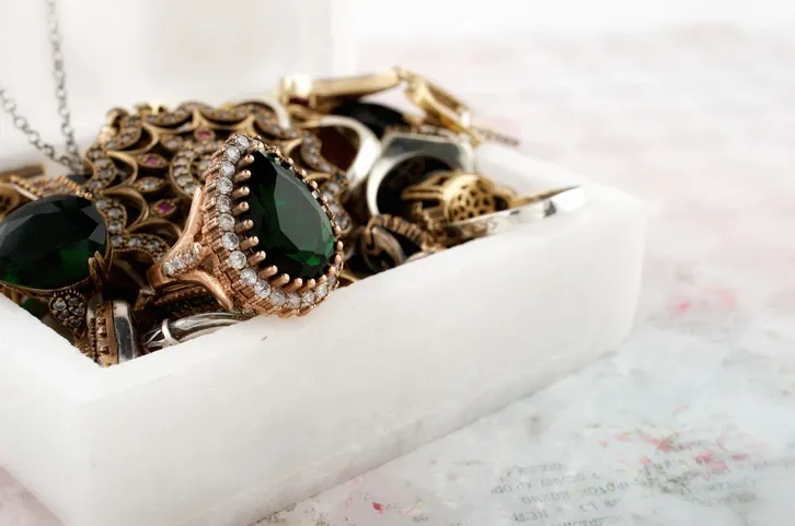 A box filled with vintage and ornate jewelry pieces, highlighting an emerald ring.