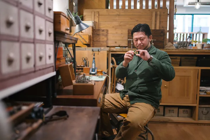 A craftsman or jeweler in a workshop, examining a piece of jewelry or a gemstone, showcasing the detailed and skilled work involved in jewelry making and assessment.