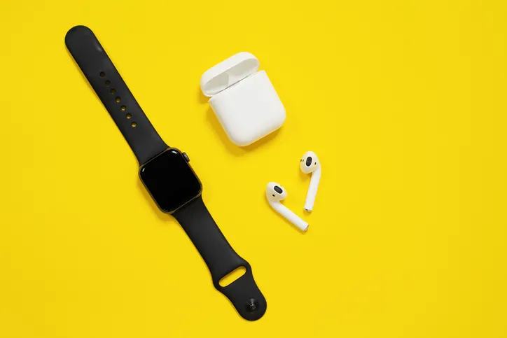 An Apple watch and AirPods laying on a yellow background.