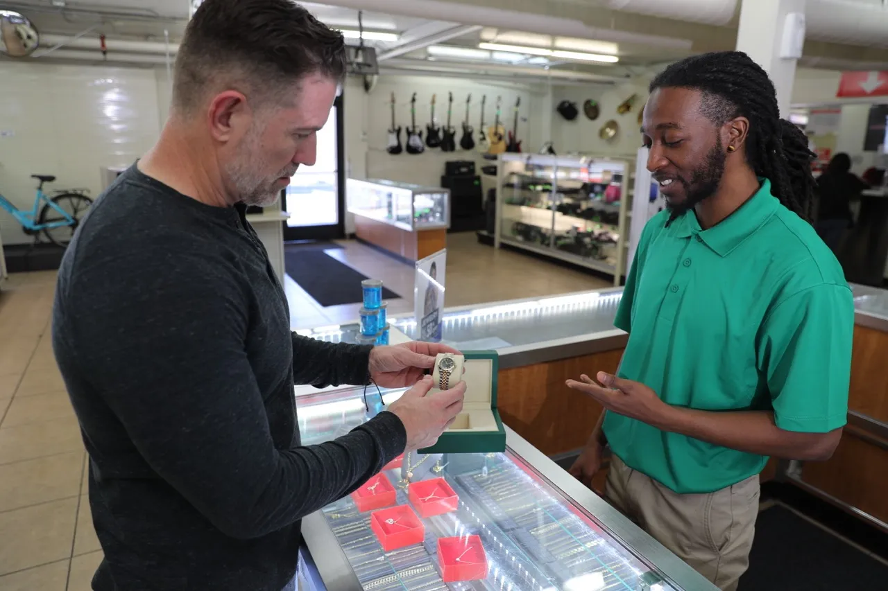 A customer is trying to pawn a Rolex watch while a Value Pawn Team Member assists with this transaction.