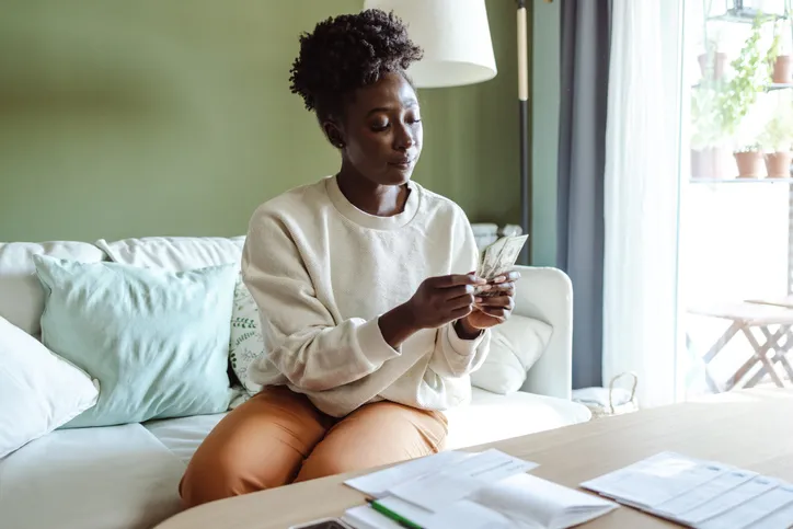 A wide shot of a woman counting cashing while sitting in a living room on a couch.